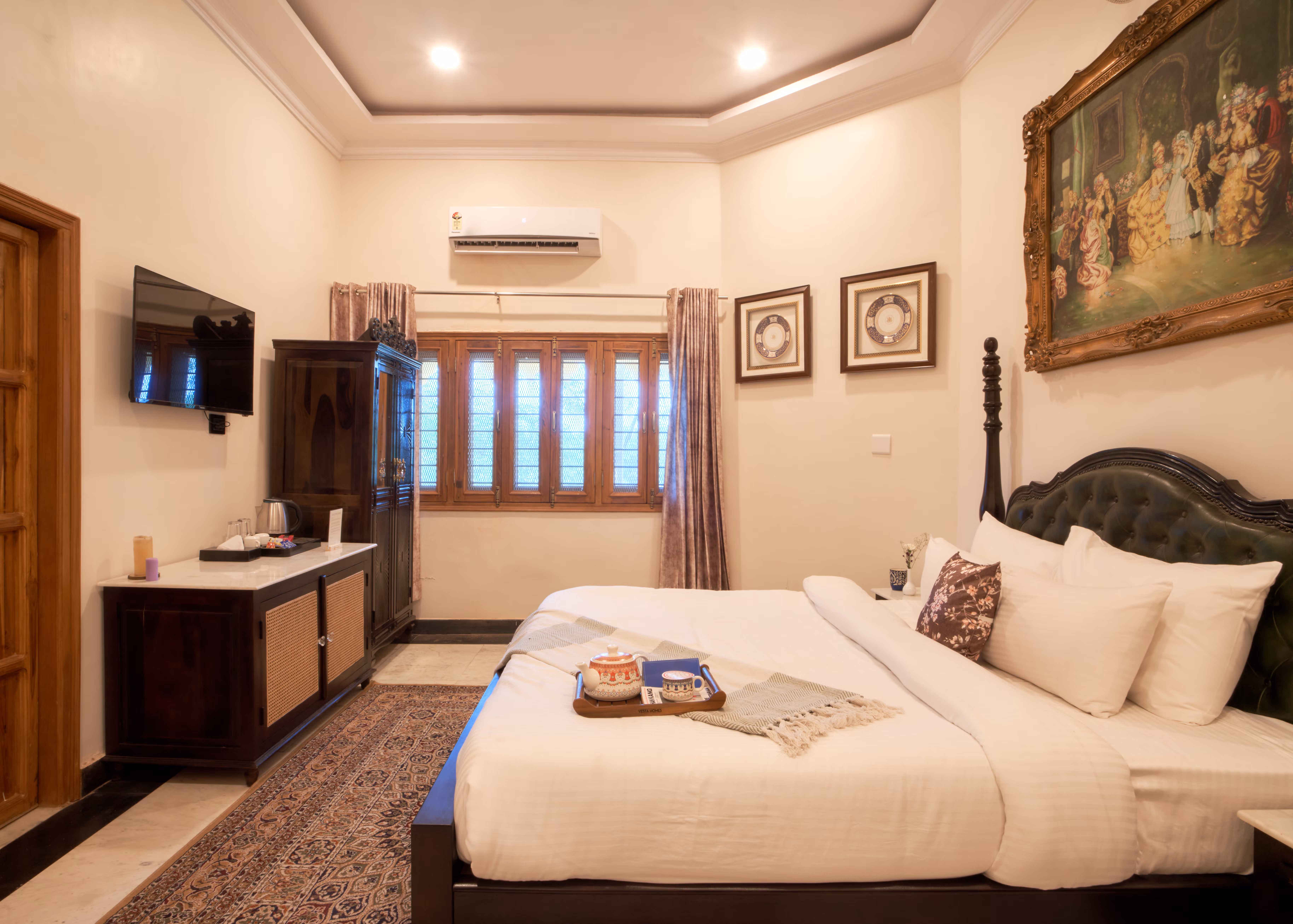 Bedroom with a carved bed, white bedding, wall-mounted television, air conditioner and curtained wooden windows.
