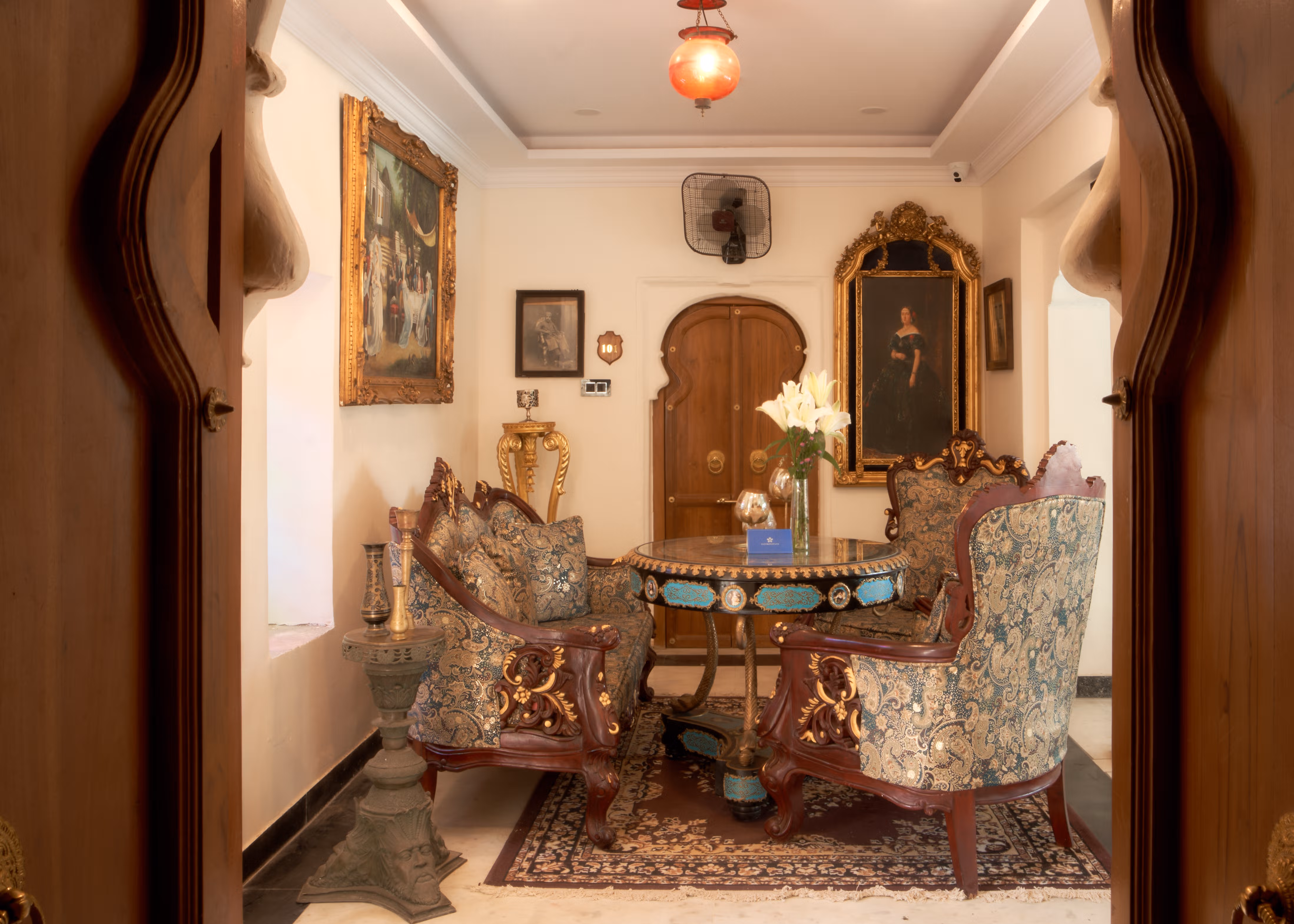 Round games table surrounded by ornate upholstered chairs, viewed through a curved palace doorway.