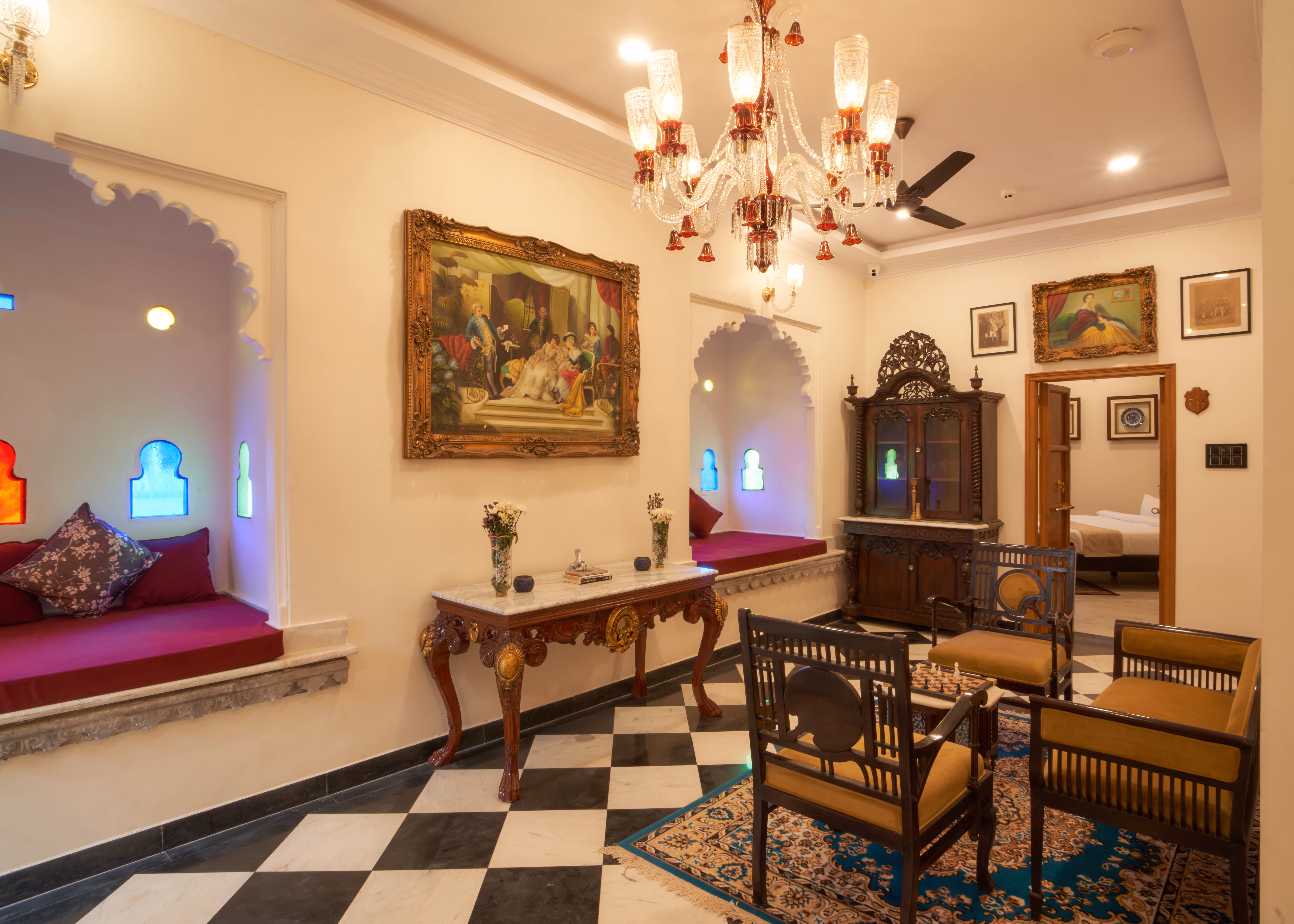 Lounge with scalloped window alcoves, magenta cushions, a chandelier and carved wooden furniture.