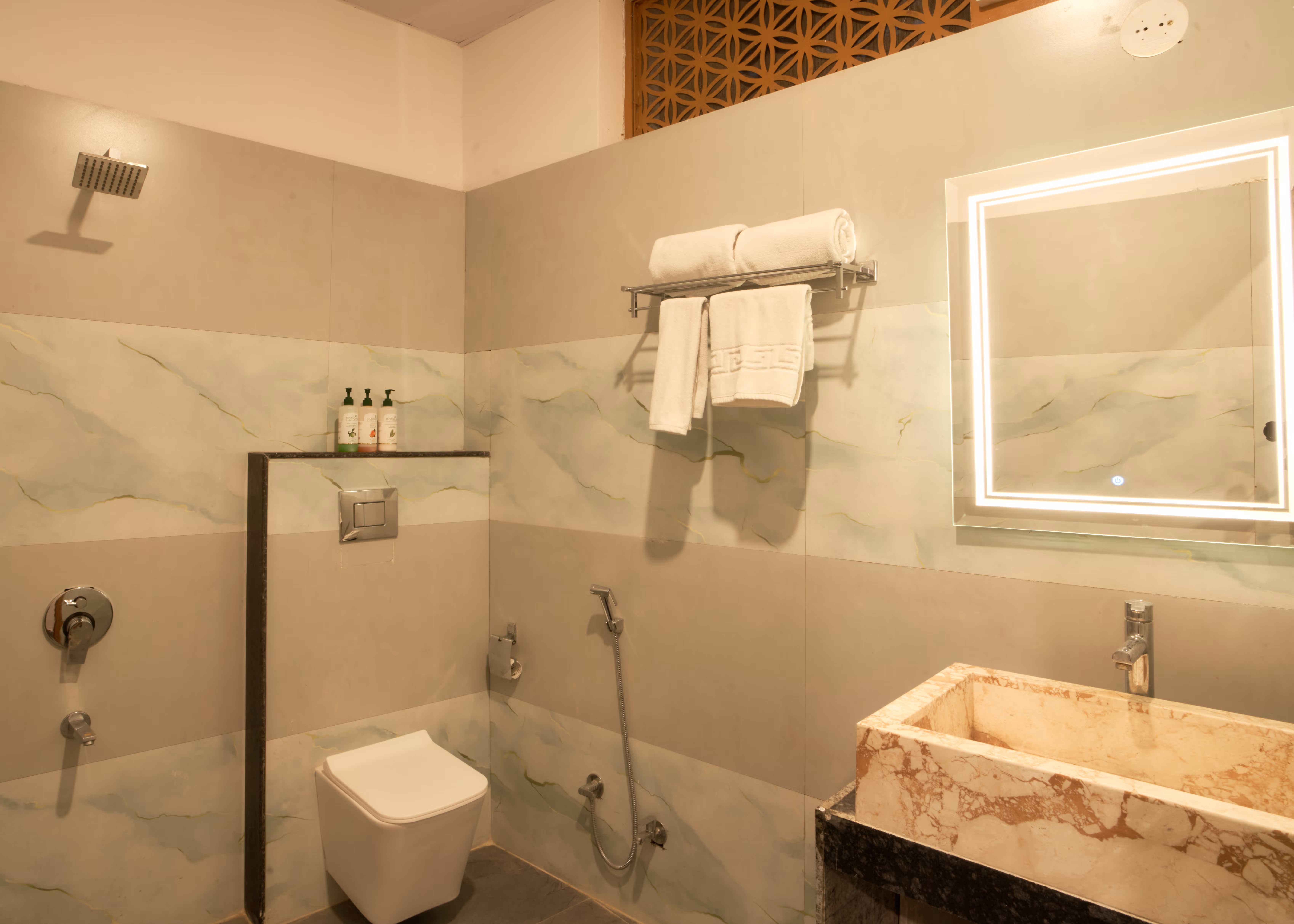 Bathroom with pale marble-patterned walls, a stone basin, illuminated mirror, shower area and folded towels.