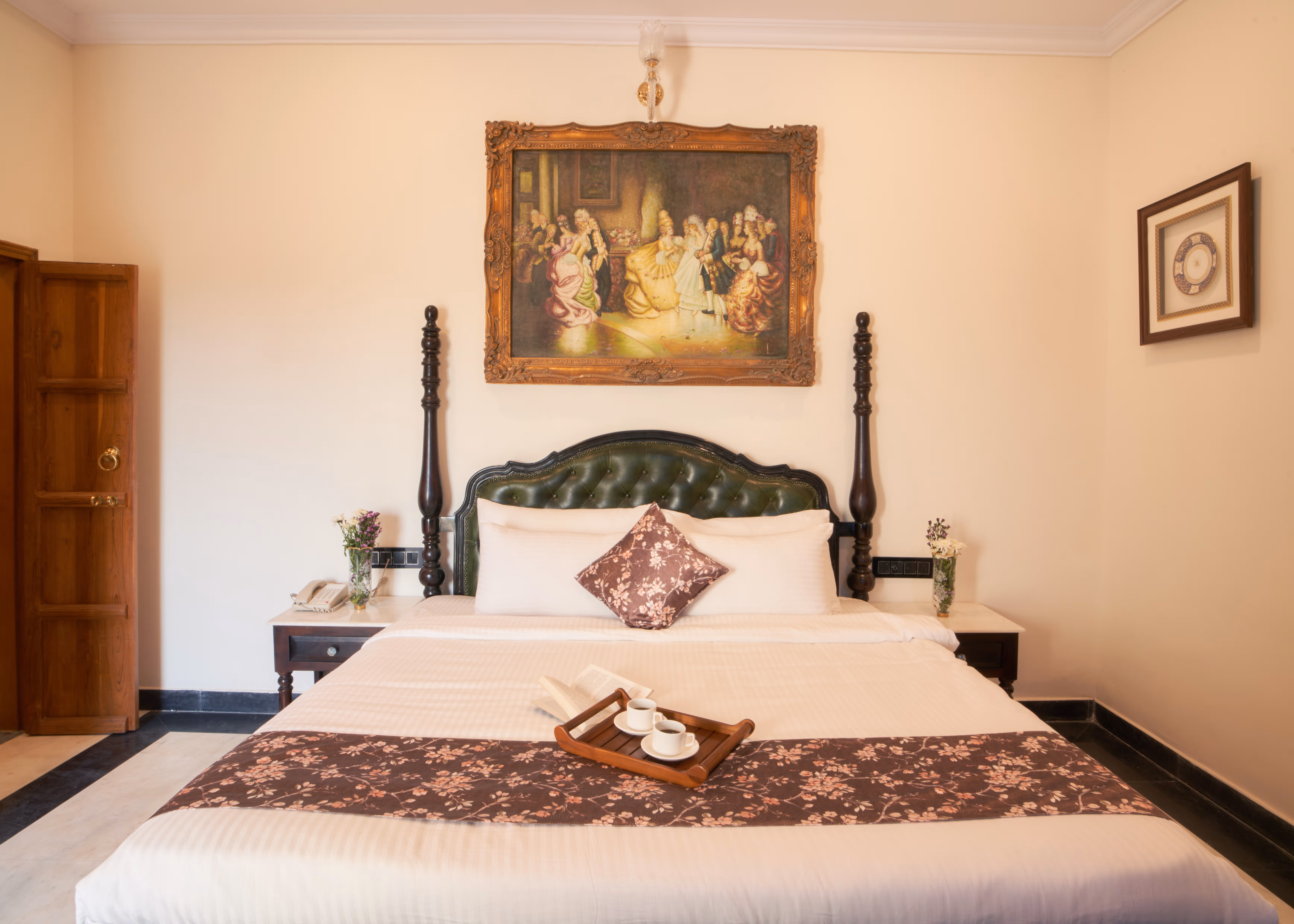 Bedroom with white bedding, a patterned maroon runner, a carved wooden headboard and a large painting above the bed.