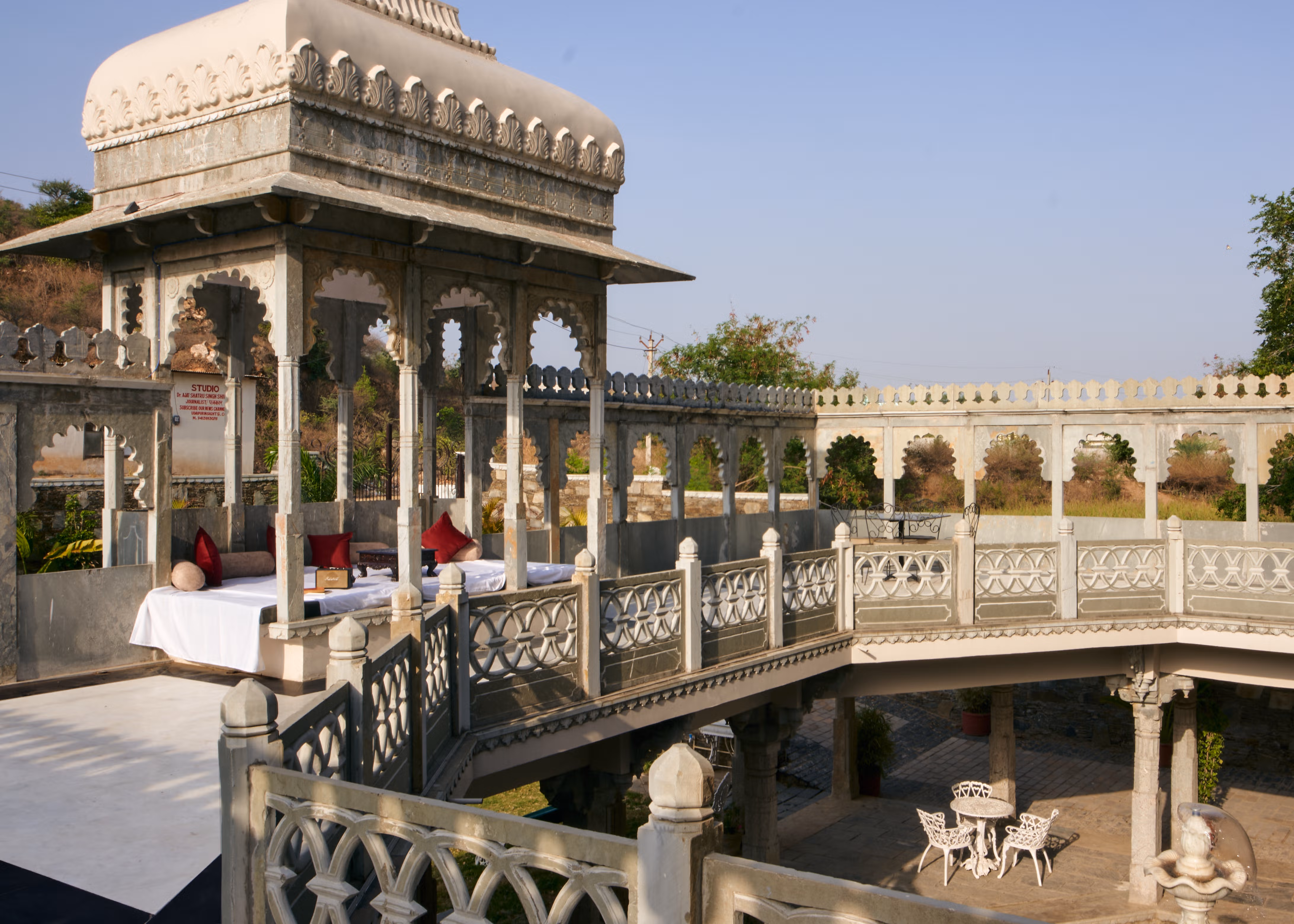 Cushioned daybed beneath a carved stone pavilion overlooking the palace courtyard and fountain.