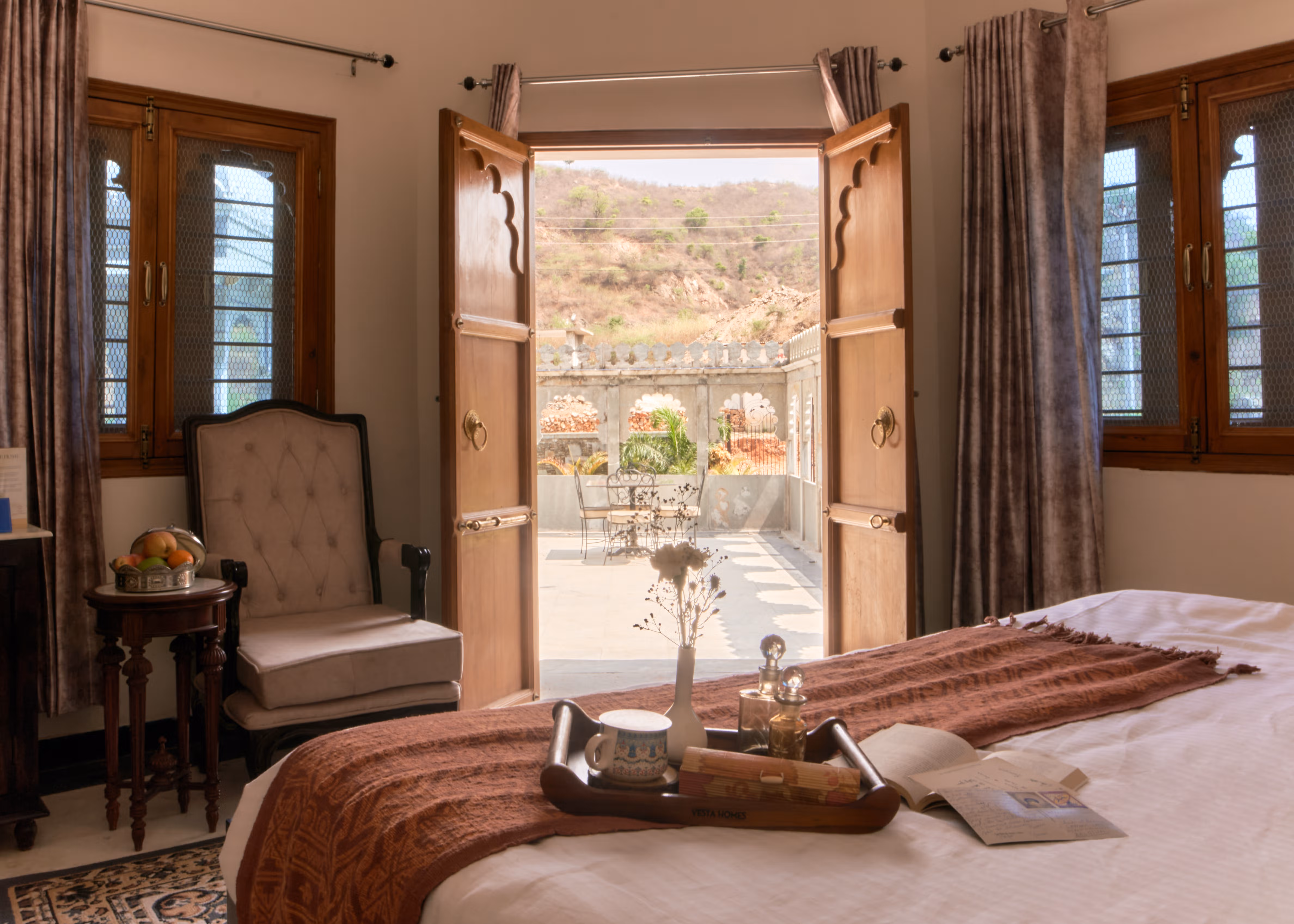 Bedroom with an upholstered armchair and open wooden doors overlooking the courtyard fountain.
