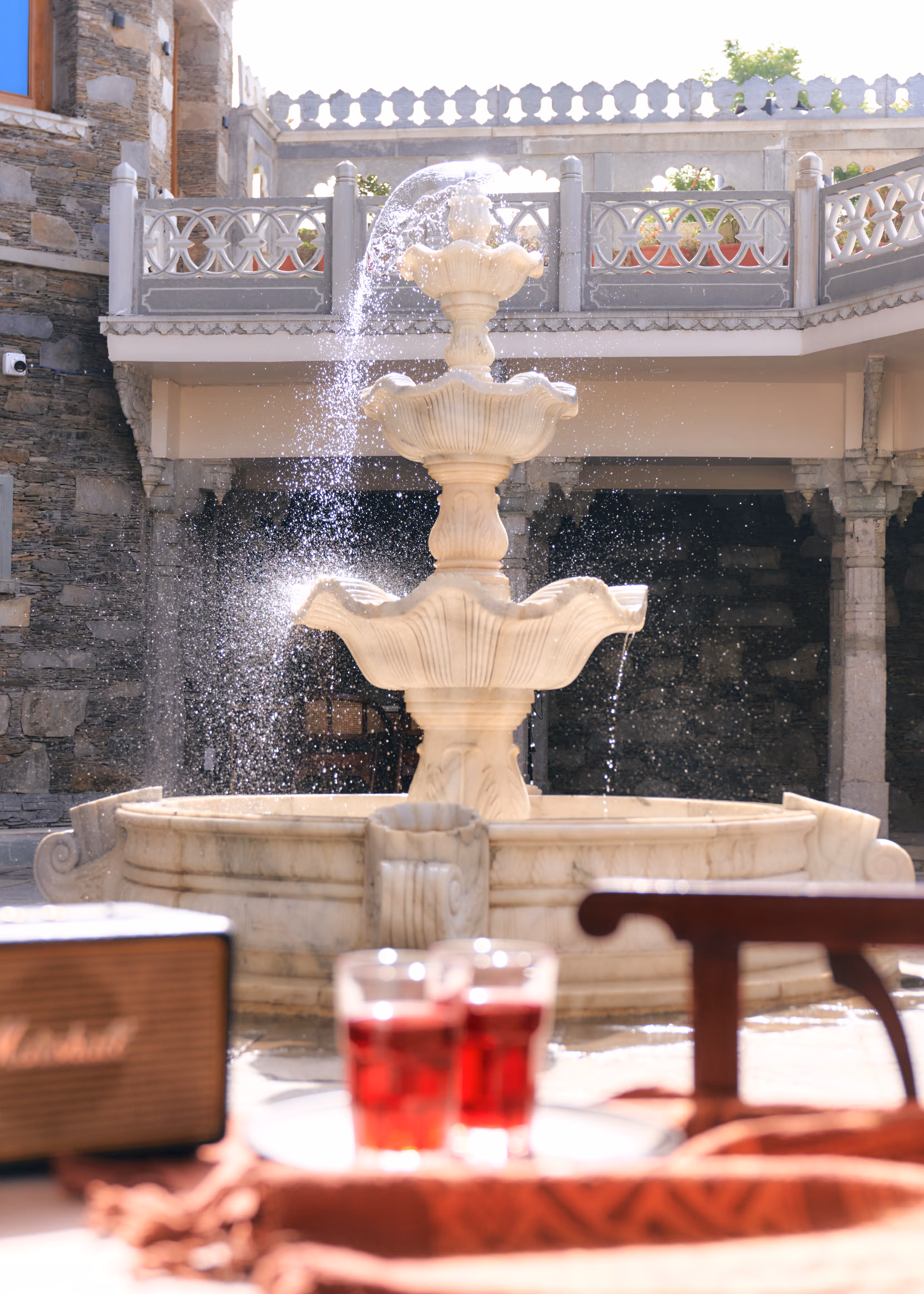Close view of water cascading from a tiered pale stone fountain against the palace’s dark stone courtyard walls.
