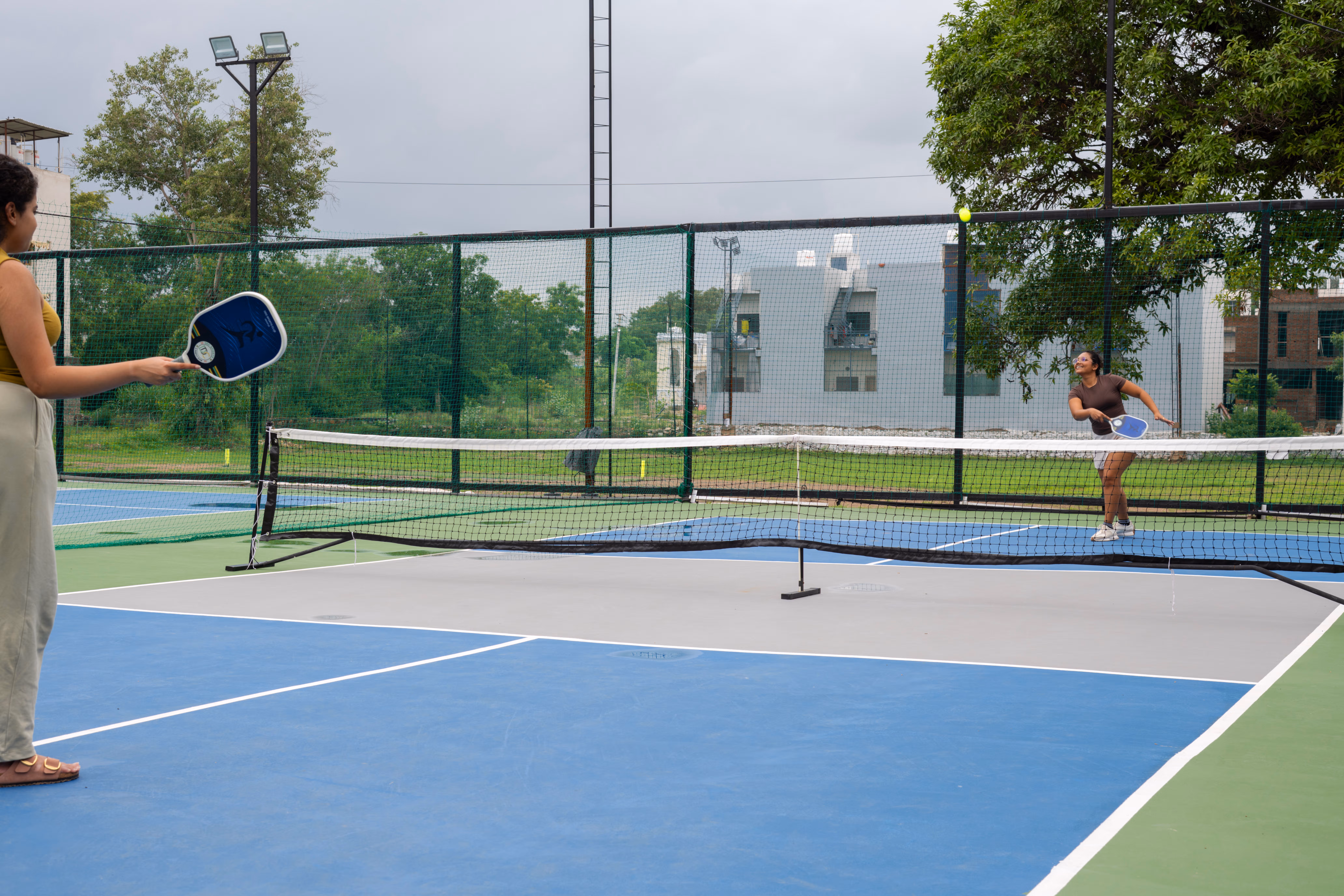 Two guests playing paddle sport on a fenced outdoor court with a blue playing surface.