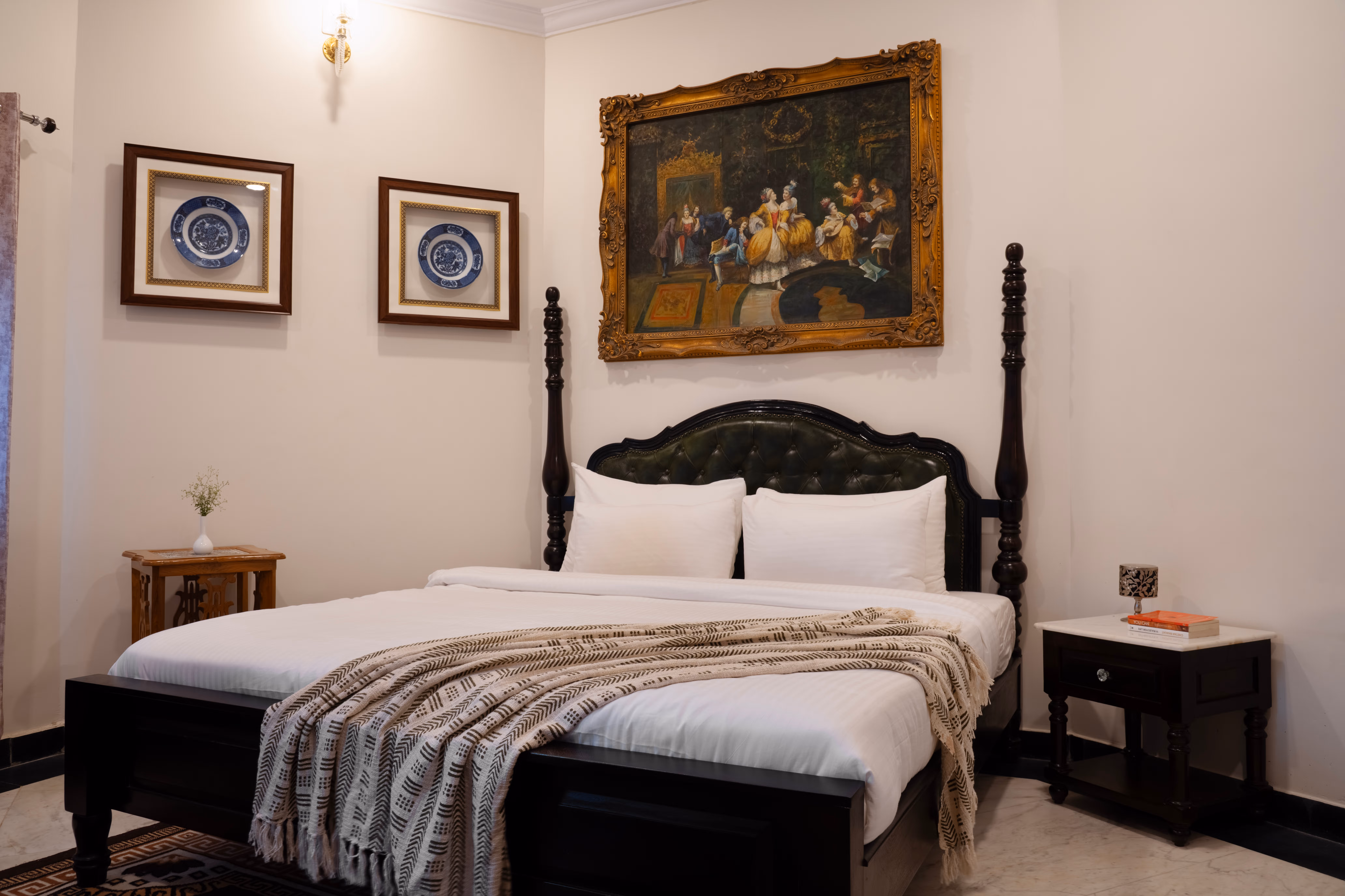 Bedroom with white bedding, a striped throw, a carved dark wooden headboard and framed artwork above the bed.