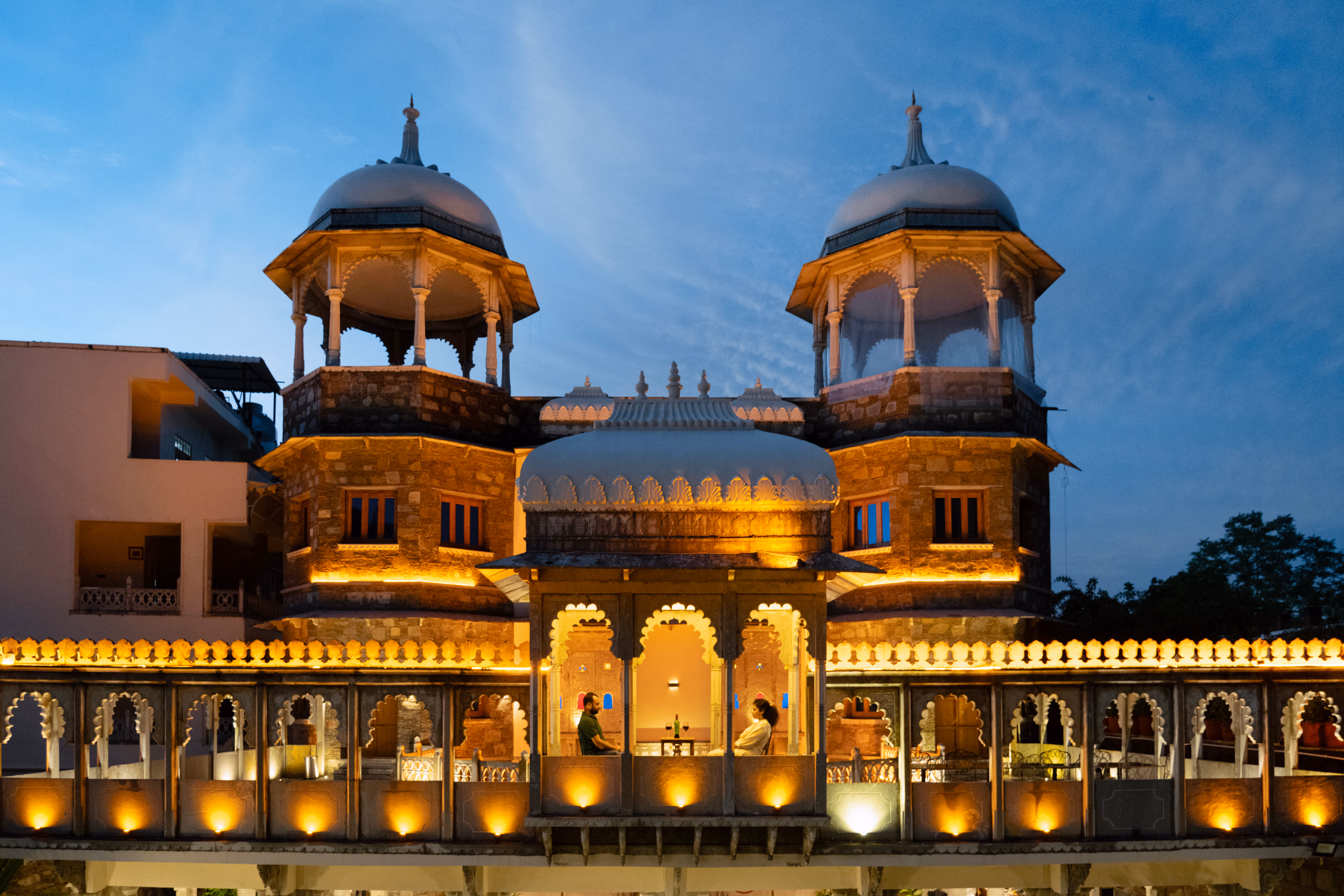 Two rooftop pavilions and an illuminated arched terrace at Shikargarh Palace beneath a blue evening sky.