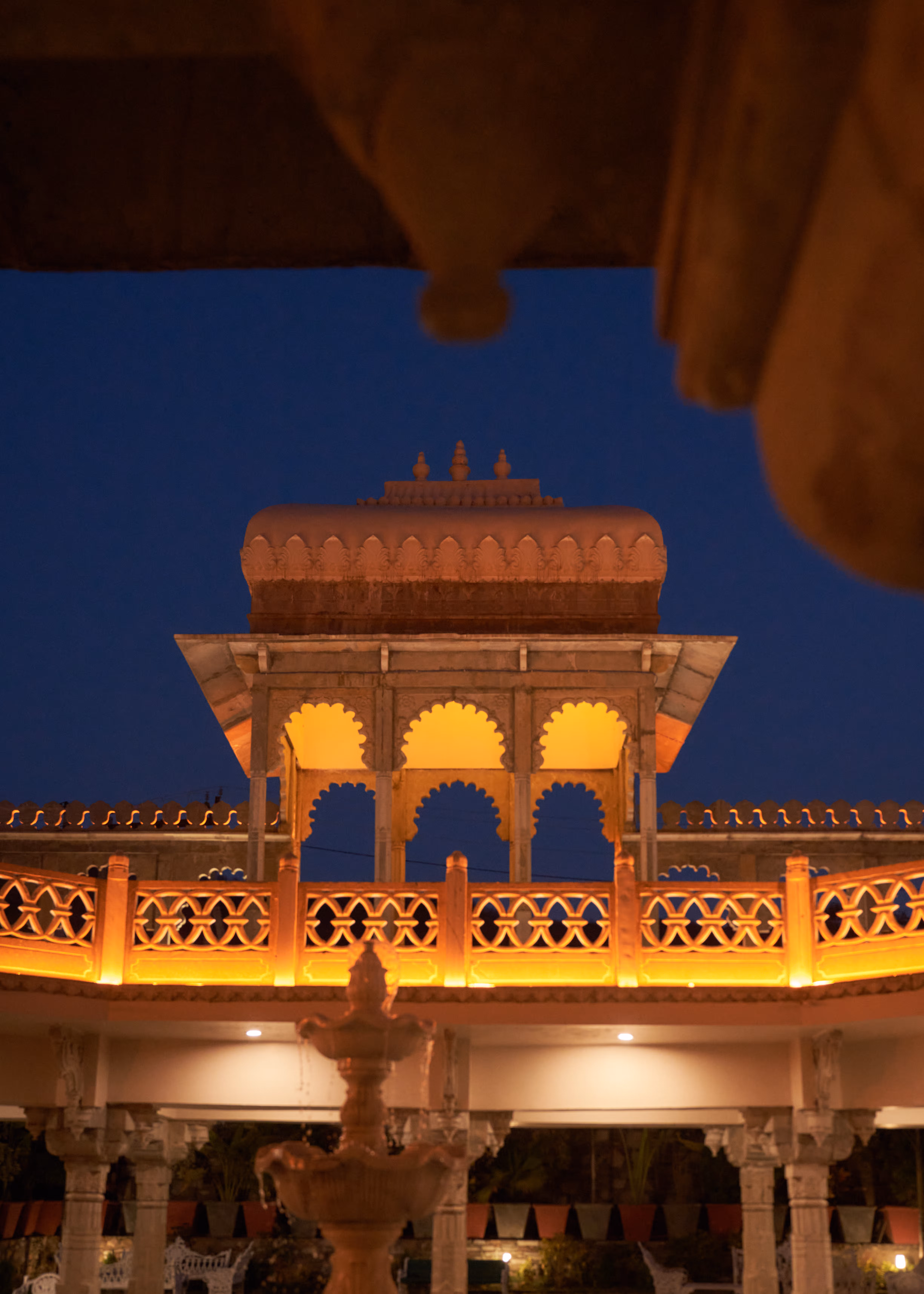 Stone pavilion with scalloped arches and decorative roof detailing illuminated against the night sky.