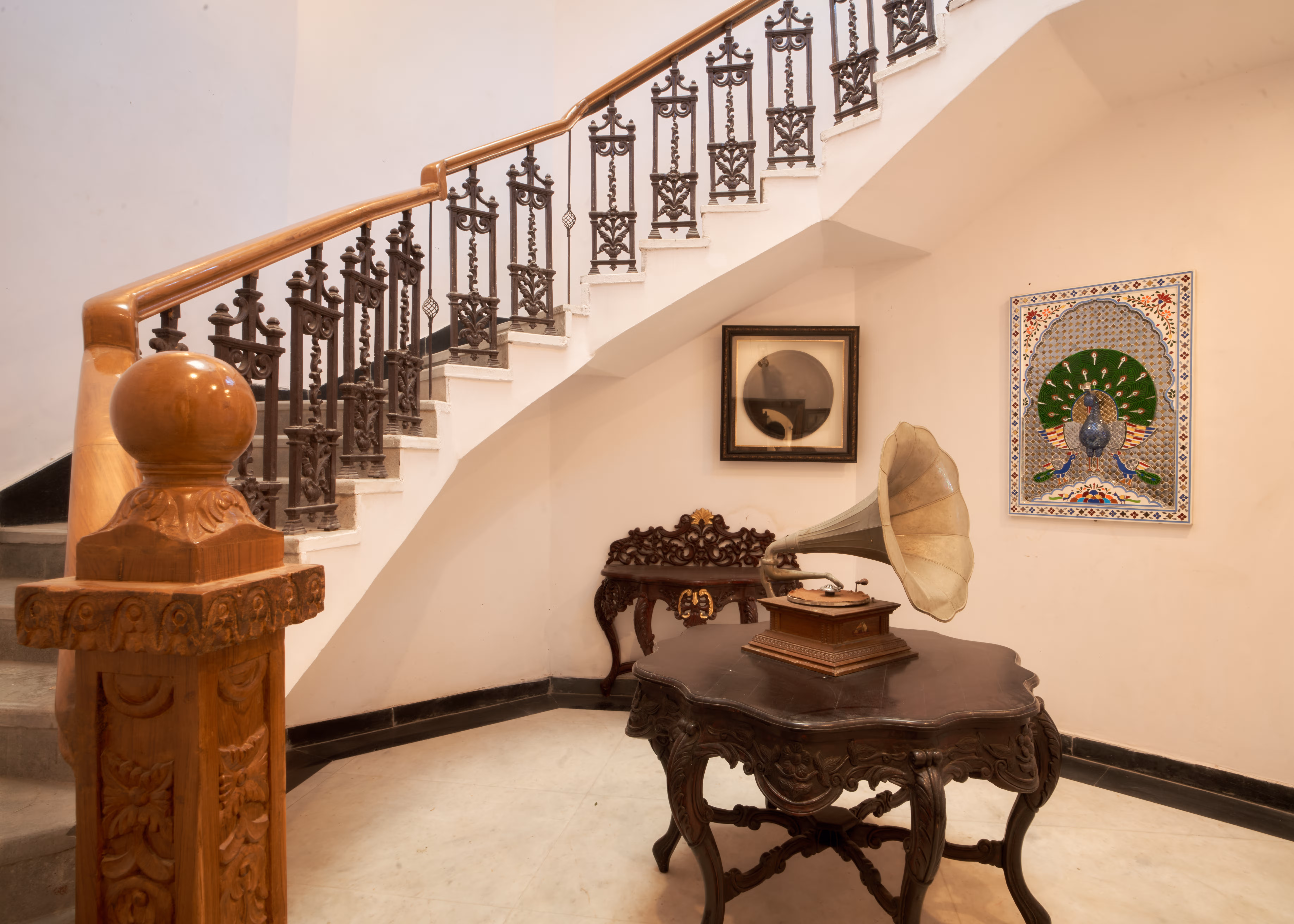Palace staircase with decorative metal railings, framed artwork and an antique-style gramophone on a wooden table.