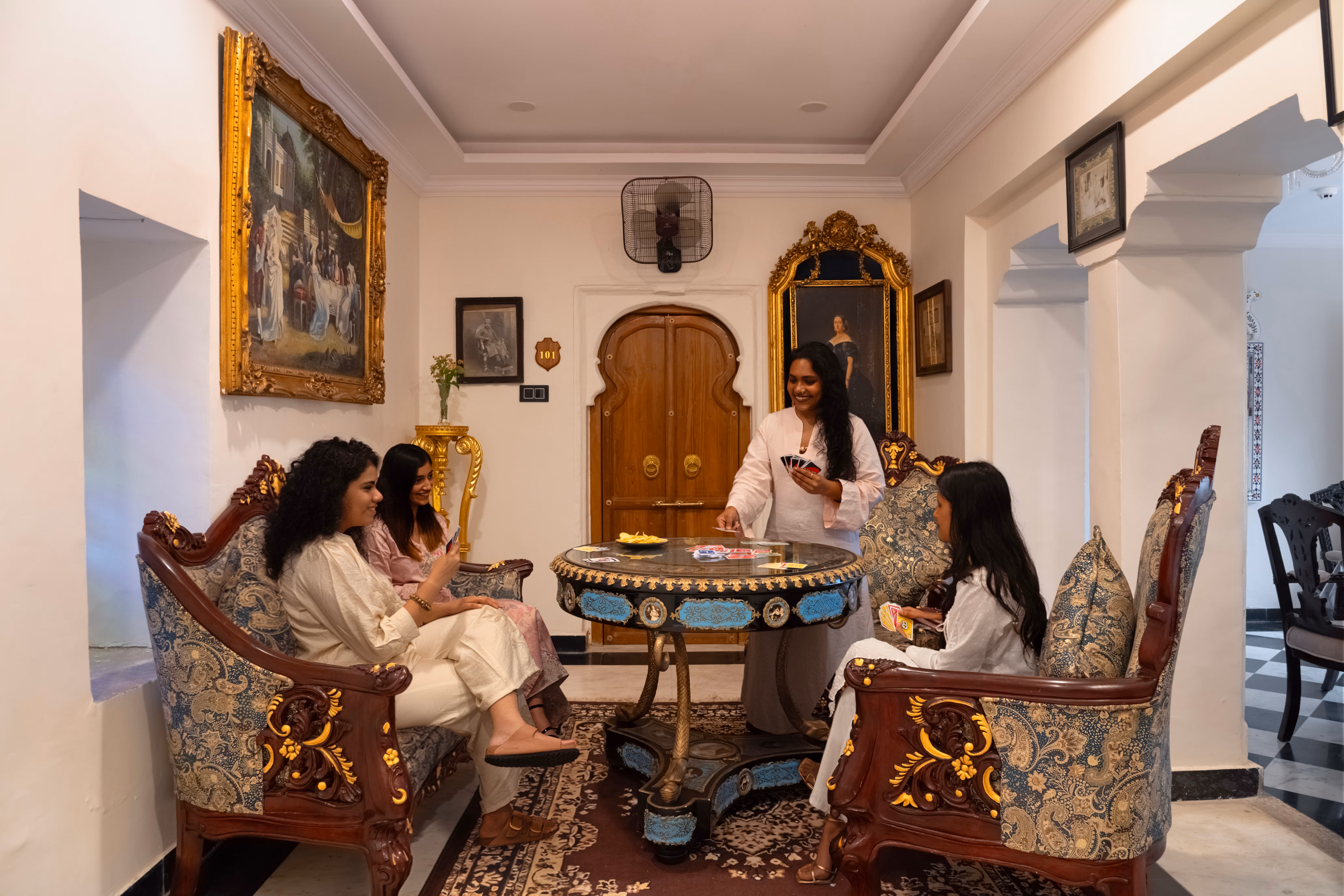 Guests gathered around a round games table with ornate upholstered chairs and heritage artwork.
