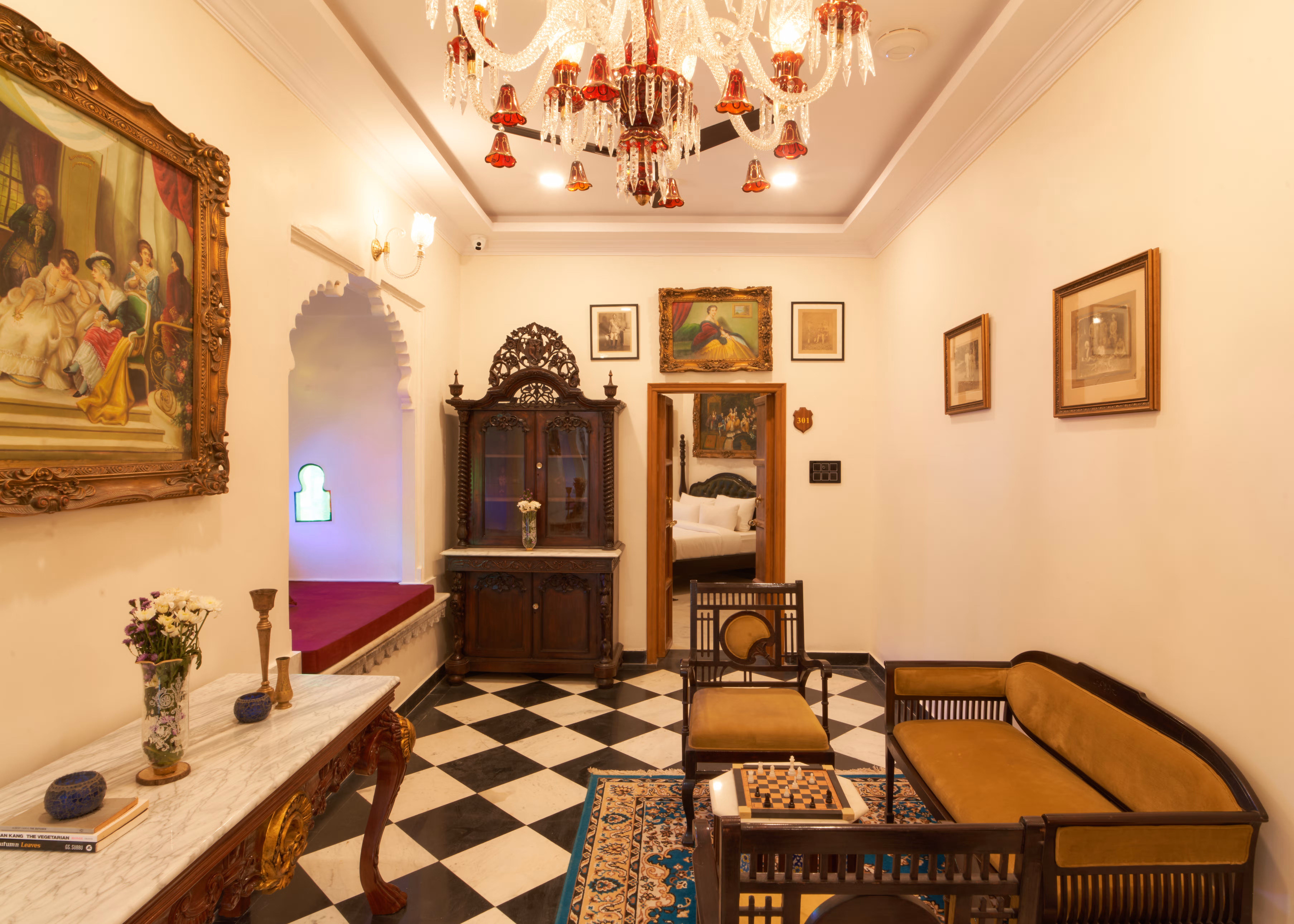 Sitting room with wooden armchairs, a decorative cabinet, framed artwork and a black-and-white tiled floor.