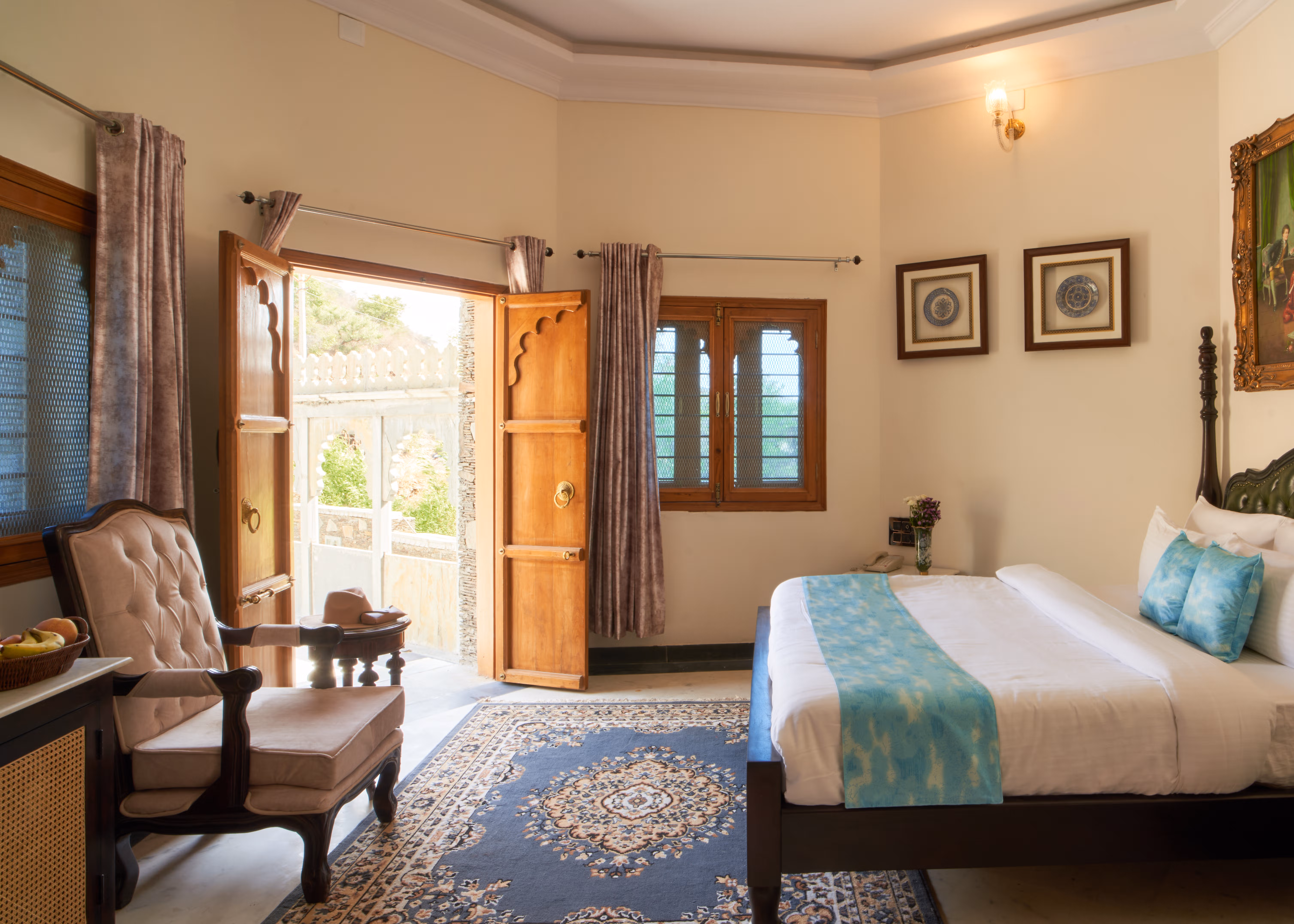 Bedroom with white bedding, turquoise accents, an upholstered armchair and open wooden doors.