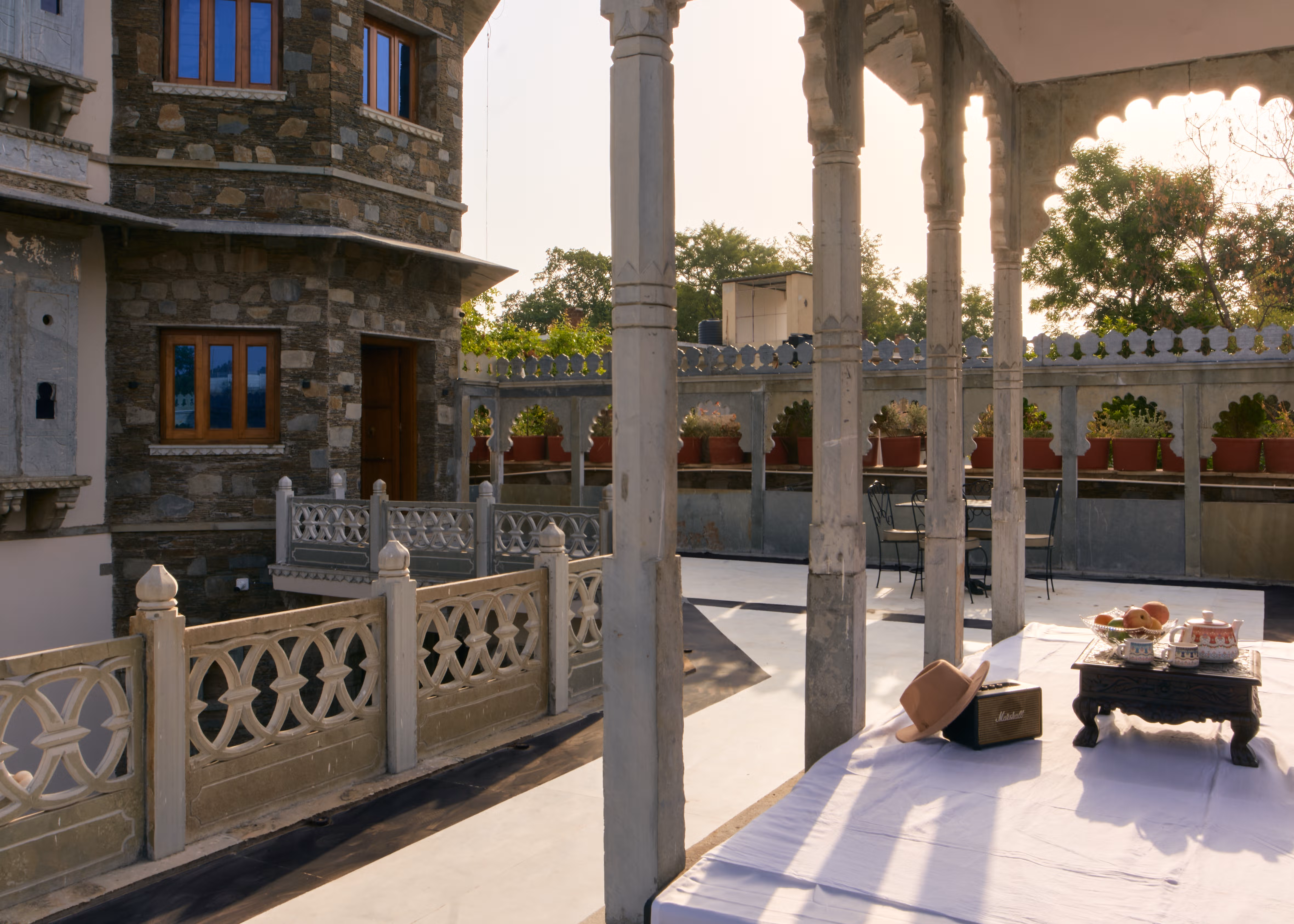 Stone terrace with carved railings and cushioned seating beneath a columned pavilion.