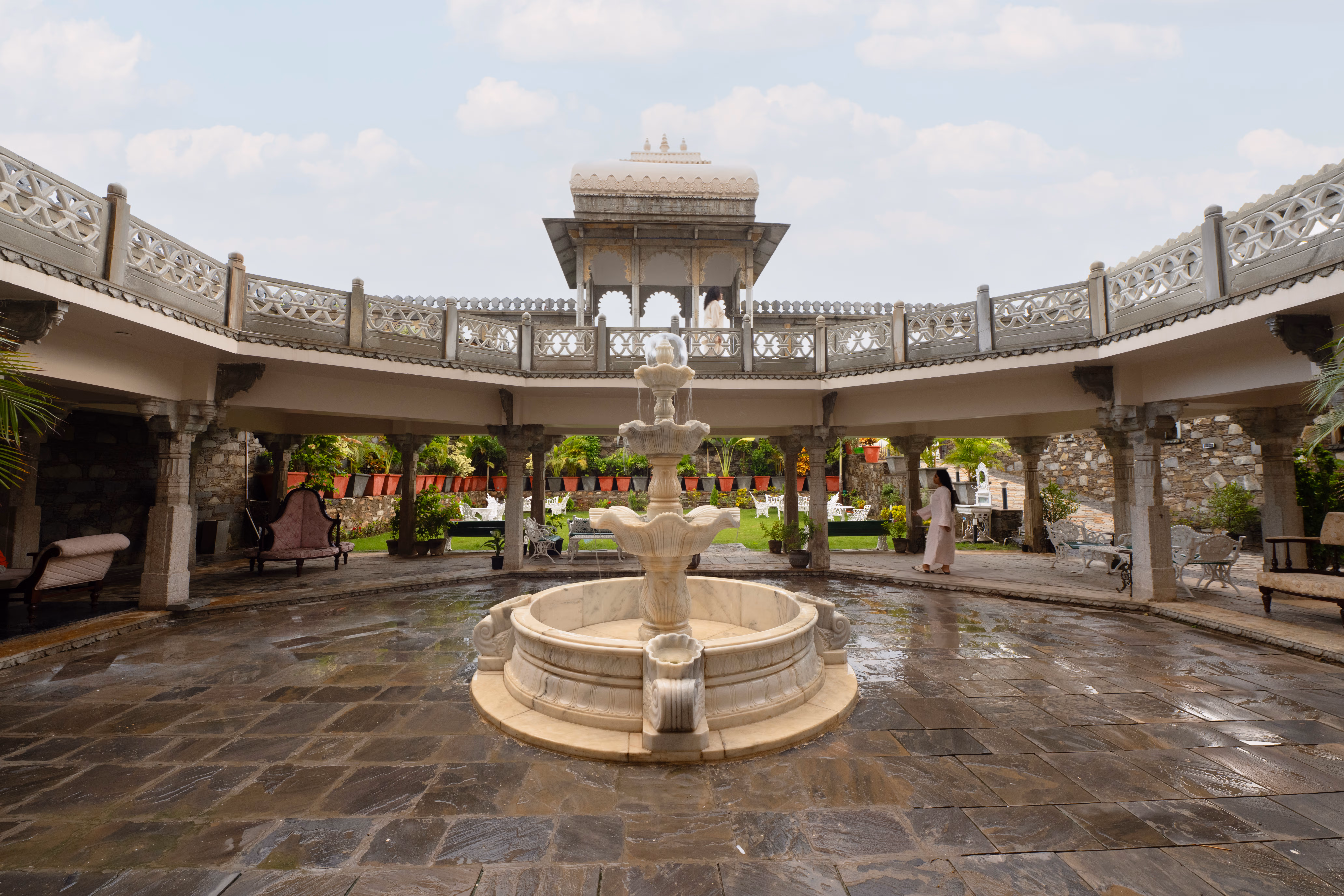 Open stone courtyard centred on a tiered fountain, with a surrounding colonnade and carved upper balcony.
